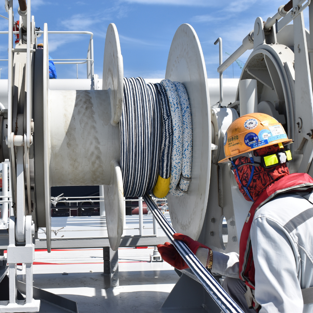 Marine worker conducting mooring equipment inspection on a ship deck, focusing on rope integrity and operational efficiency under international maritime safety standards.