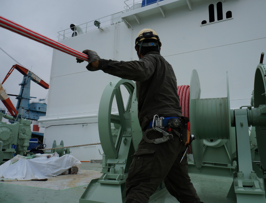 Marine worker handling mooring rope installation on a ship deck, ensuring compliance with international mooring safety standards and operational efficiency.